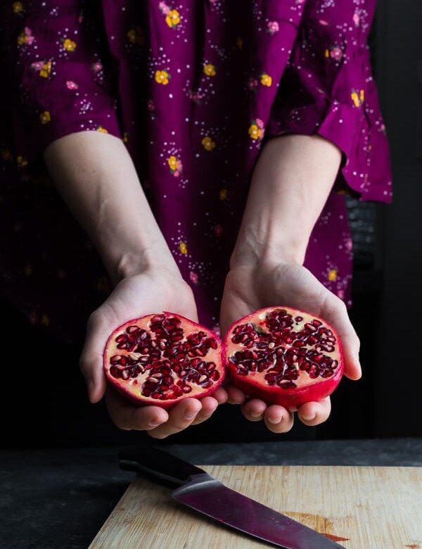 hand holding out a pomegranate cut in half