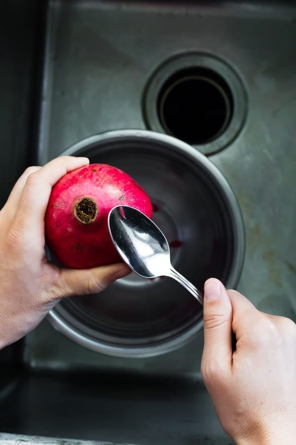 a cut pomegranate being hit with a spoon