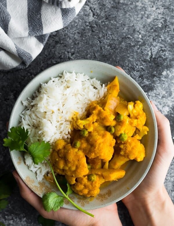hands holding a white bowl filled with cauliflower korma and rice