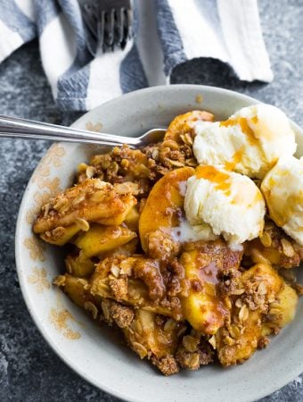 white bowl filled with apple crisp with ice cream and a spoon