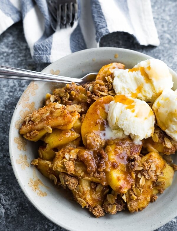 white bowl filled with apple crisp with ice cream and a spoon
