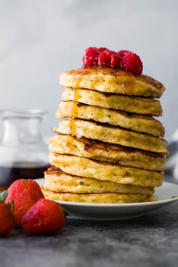 Side view of stack of cottage cheese pancakes on white plate with syrup and raspberries