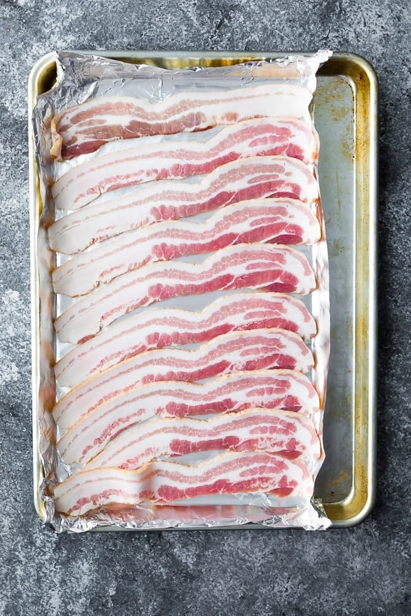 uncooked bacon arranged in a single layer on foil on a sheet pan