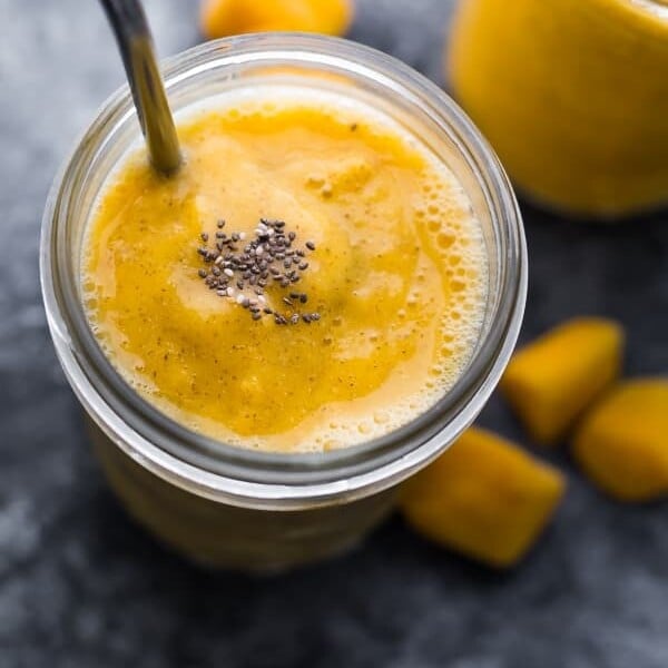 mango smoothie in a glass mason jar with chunks of mango in the background