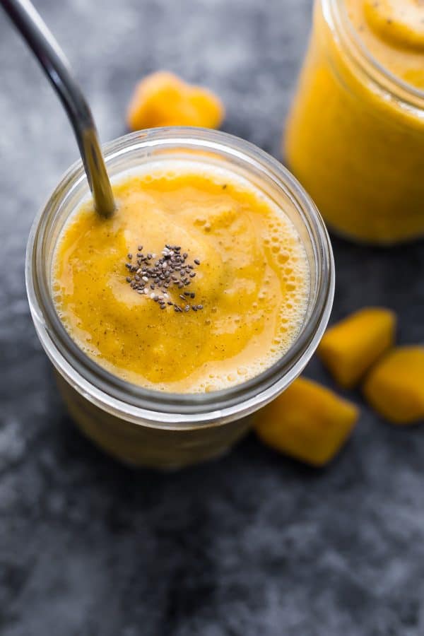 mango smoothie in a glass mason jar with chunks of mango in the background