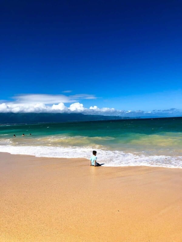 a boy sitting on the beach in maui