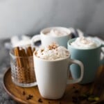three cups of chai tea latte and a cup of cinnamon sticks on wood tray