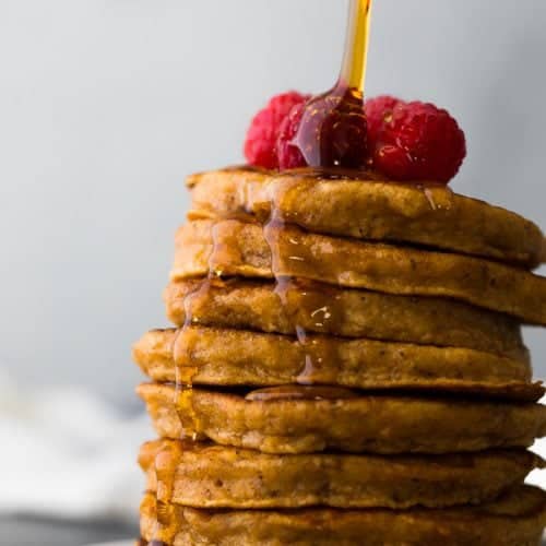 stack of sweet potato pancakes with fresh raspberries and syrup being drizzled over top