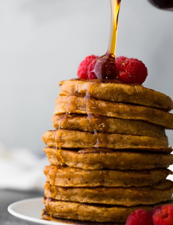 stack of sweet potato pancakes with fresh raspberries and syrup being drizzled over top