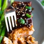 Close up shot of a fork taking off a piece of teriyaki salmon with green beans next to it