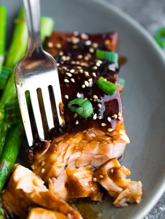 Close up shot of a fork taking off a piece of teriyaki salmon with green beans next to it