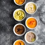 overhead shot of 7 different hummus recipes in white bowls