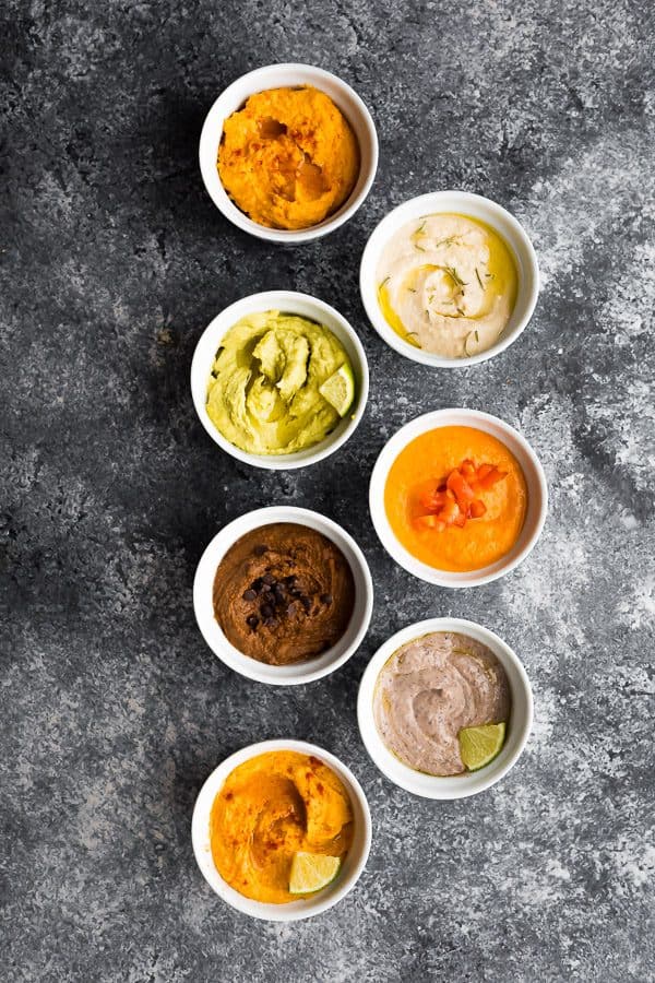 overhead shot of 7 different hummus recipes in white bowls