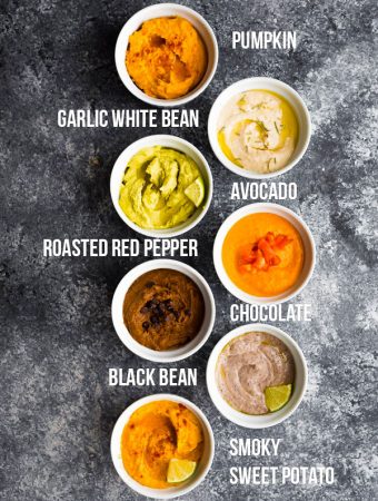 overhead shot of 7 different hummus recipes in white bowls with labels