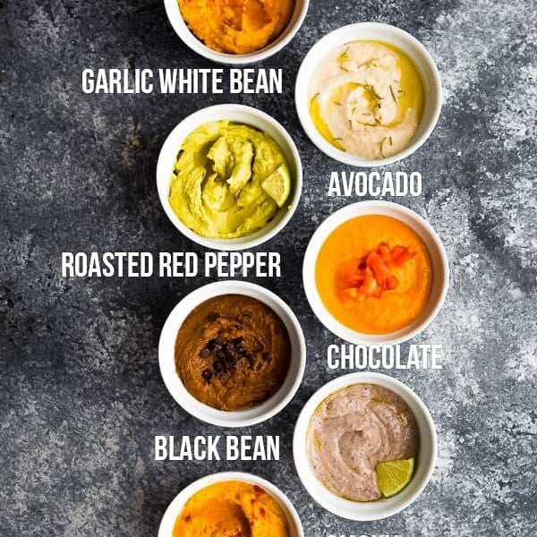 overhead shot of 7 different hummus recipes in white bowls with labels