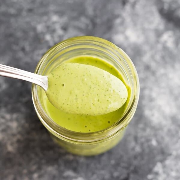 spoonful of green goddess dressing over a mason jar