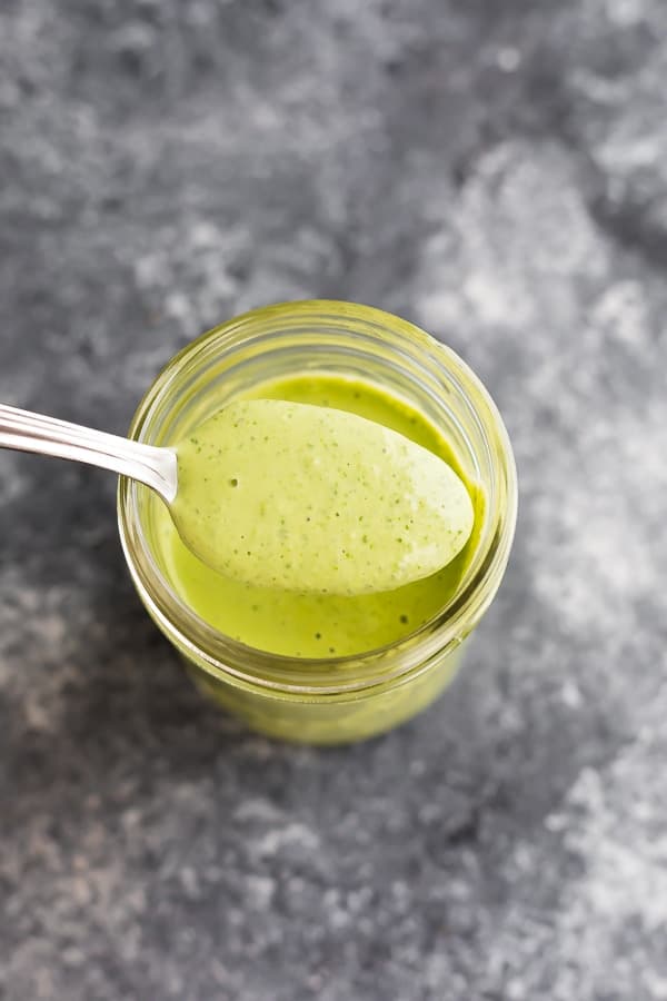 spoonful of green goddess dressing over a mason jar