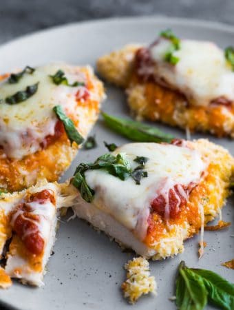 four pieces of baked chicken parmesan on gray plate with basil sprinkle