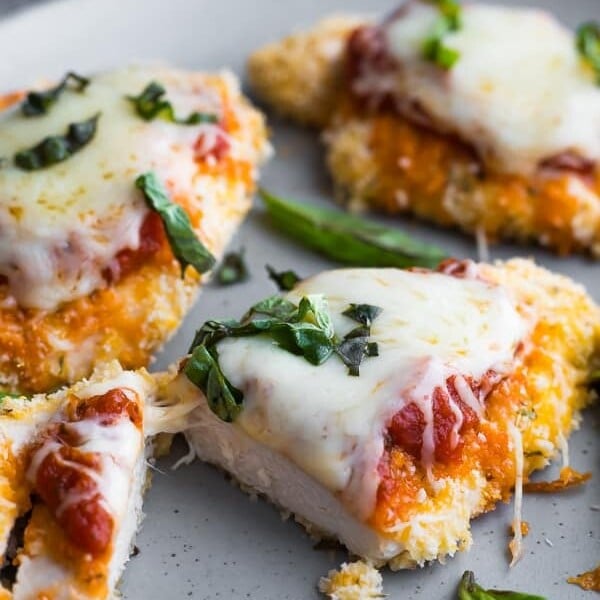 four pieces of baked chicken parmesan on gray plate with basil sprinkle