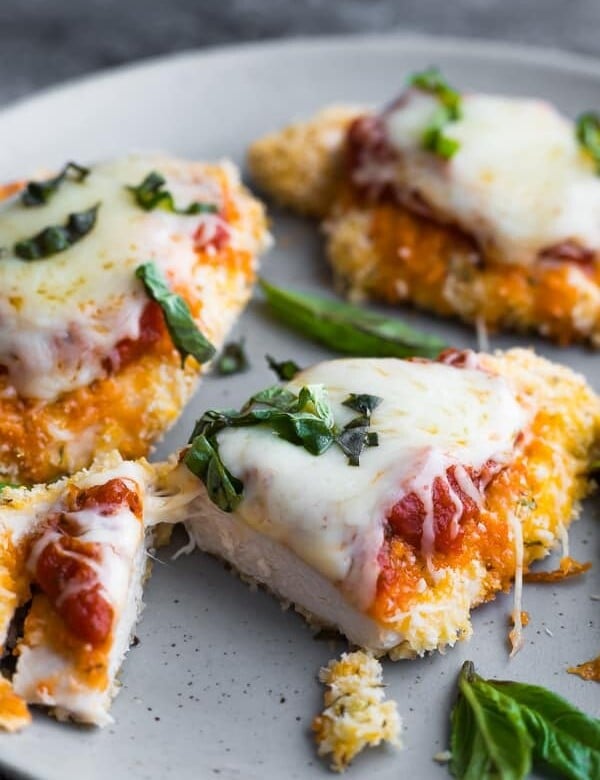 four pieces of baked chicken parmesan on gray plate with basil sprinkle