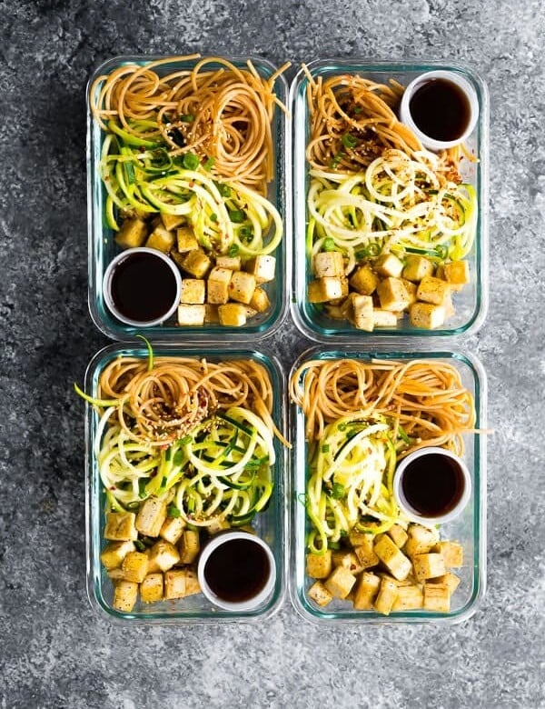 overhead shot of four spicy tofu noodle meal prep bowls in glass containers