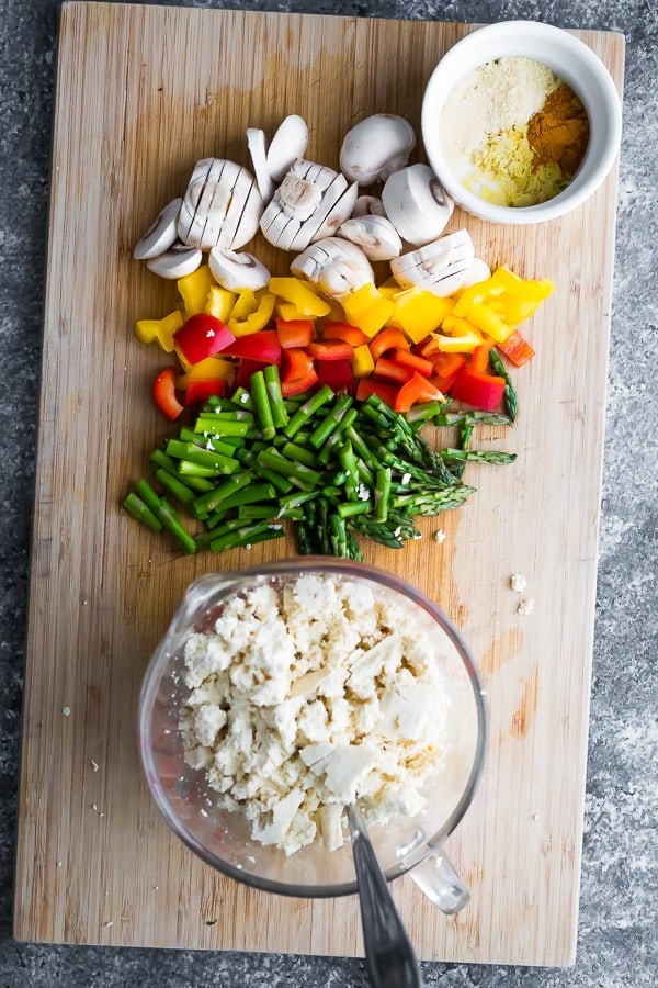 ingredients for tofu scramble recipe on cutting board, including mushrooms, bell pepper, asparagus, tofu