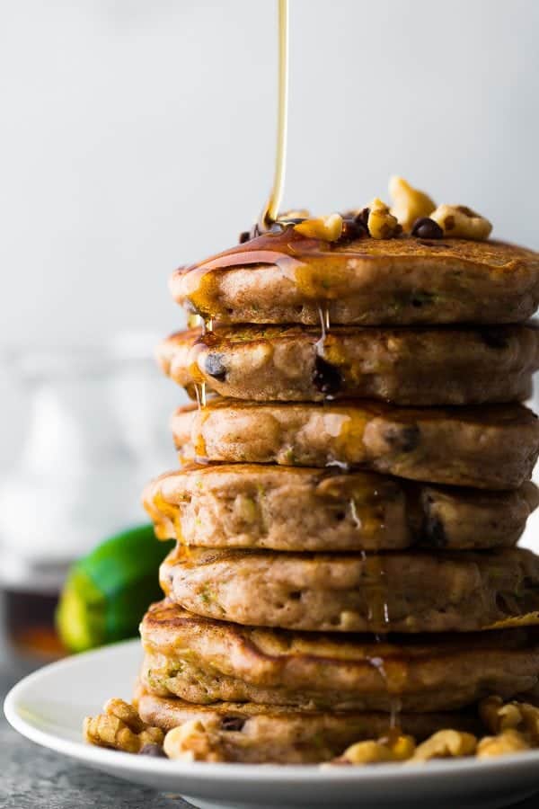 stack of zucchini chocolate chip pancakes with maple syrup being drizzled on top