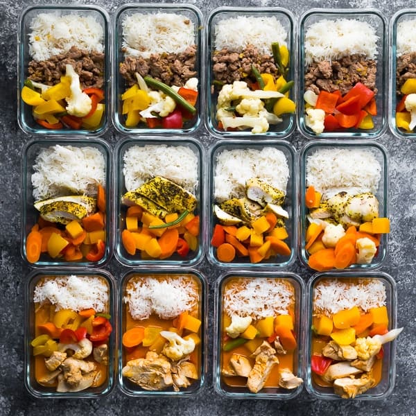 Overhead shot of twelves glass meal prep containers with variety of precooked meal options