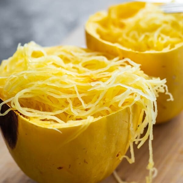 two halves of cooked spaghetti squash sitting on a wood cutting board