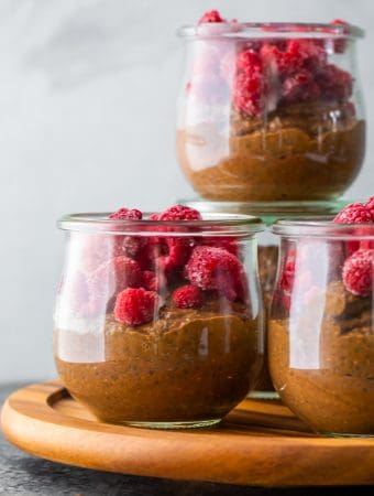Four glass cups filled with chocolate chia pudding and fresh raspberries