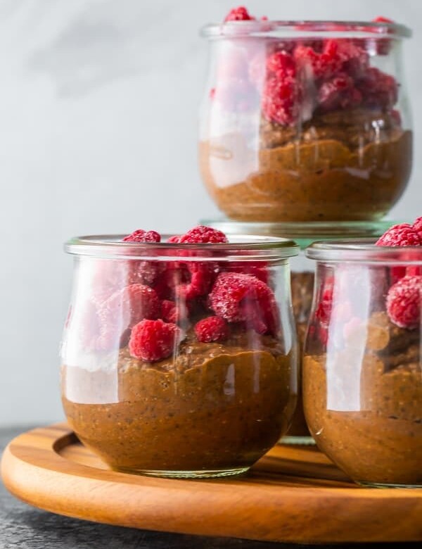 Four glass cups filled with chocolate chia pudding and fresh raspberries