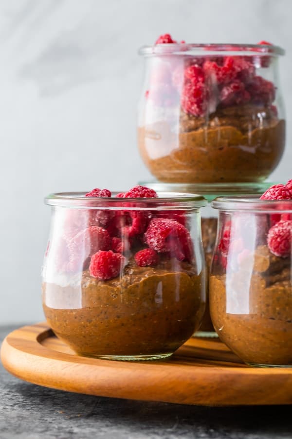 Four glass cups filled with chocolate chia pudding and fresh raspberries