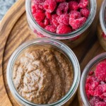 overhead shot of jars filled with chocolate chia pudding and fresh raspberries on wood board