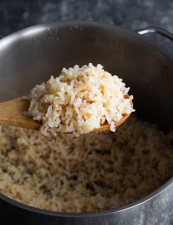 wooden spoon taking brown rice out of pot