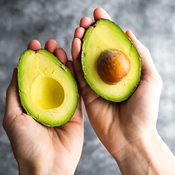 hands holding an avocado cut in half