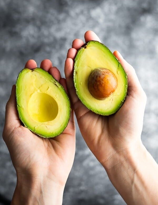 hands holding an avocado cut in half