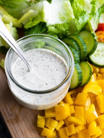 jar of healthy homemade ranch dressing with spoon in it and chopped vegetables next to it