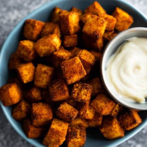 A blue bowl filled with crispy air fryer tofu and dipping sauce