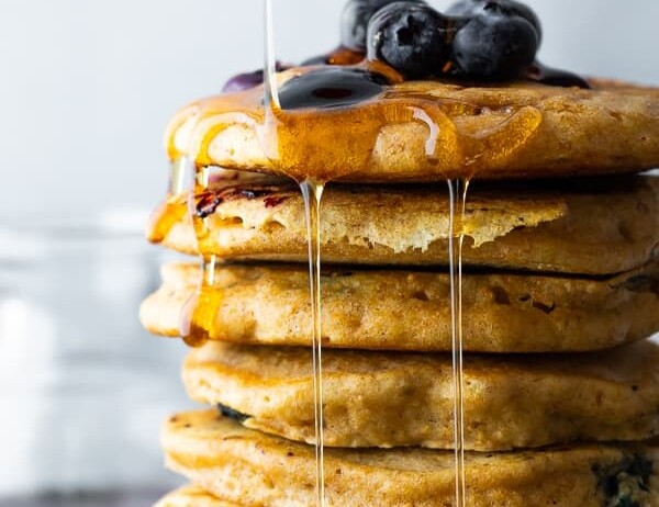 side image of stack of blueberry pancakes with syrup and fresh blueberries