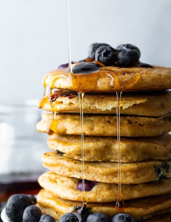 side image of stack of blueberry pancakes with syrup and fresh blueberries