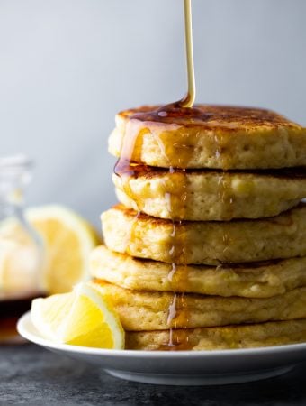 side image of stack of lemon ricotta pancakes with maple syrup drizzled and lemon slices