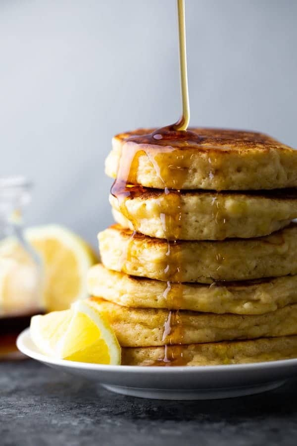 side image of stack of lemon ricotta pancakes with maple syrup drizzled and lemon slices