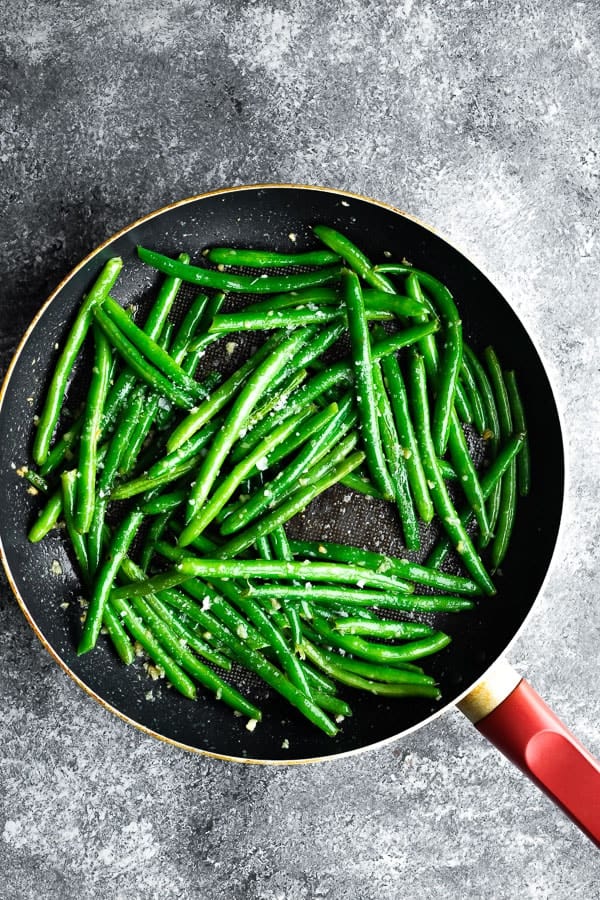 showing sauteed green beans in pan sprinkled with flaky sea salt