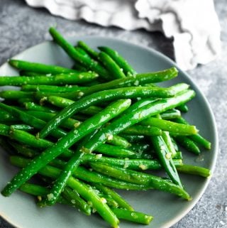 Pile of sauteed green beans with garlic butter on gray plate