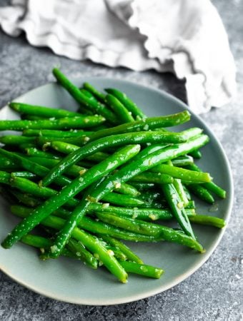 Pile of sauteed green beans with garlic butter on gray plate