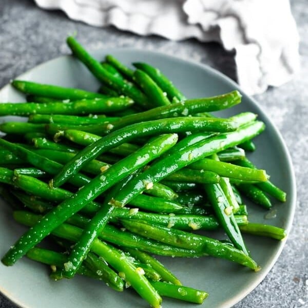Pile of sauteed green beans with garlic butter on gray plate