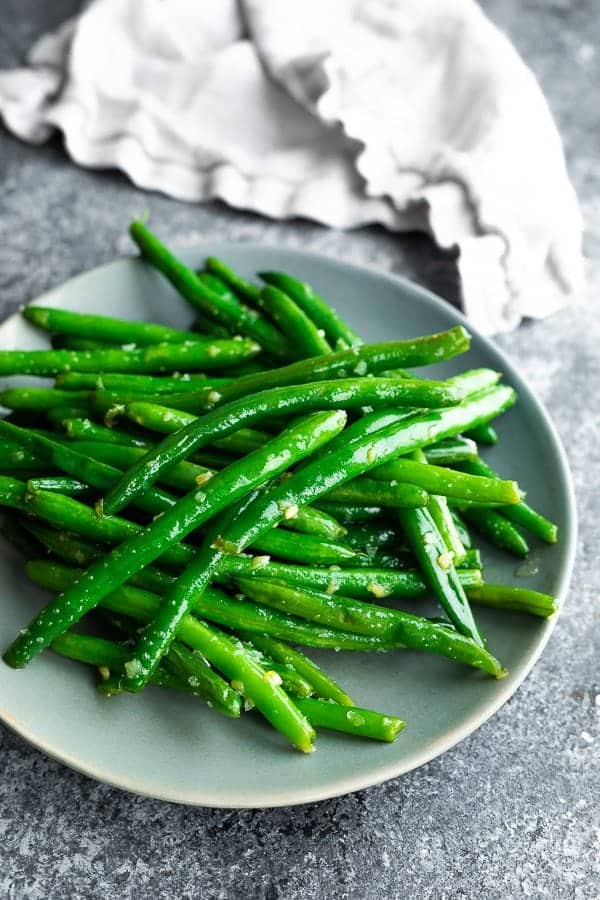 Pile of sauteed green beans with garlic butter on gray plate