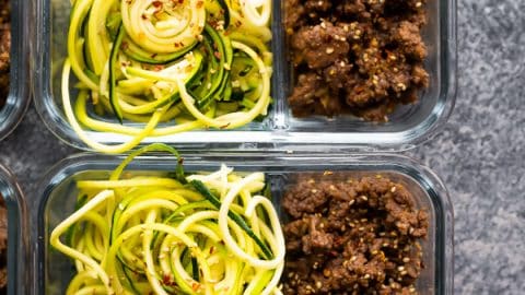 overhead shot of glass meal prep containers filled with sesame ginger beef and zucchini noodles