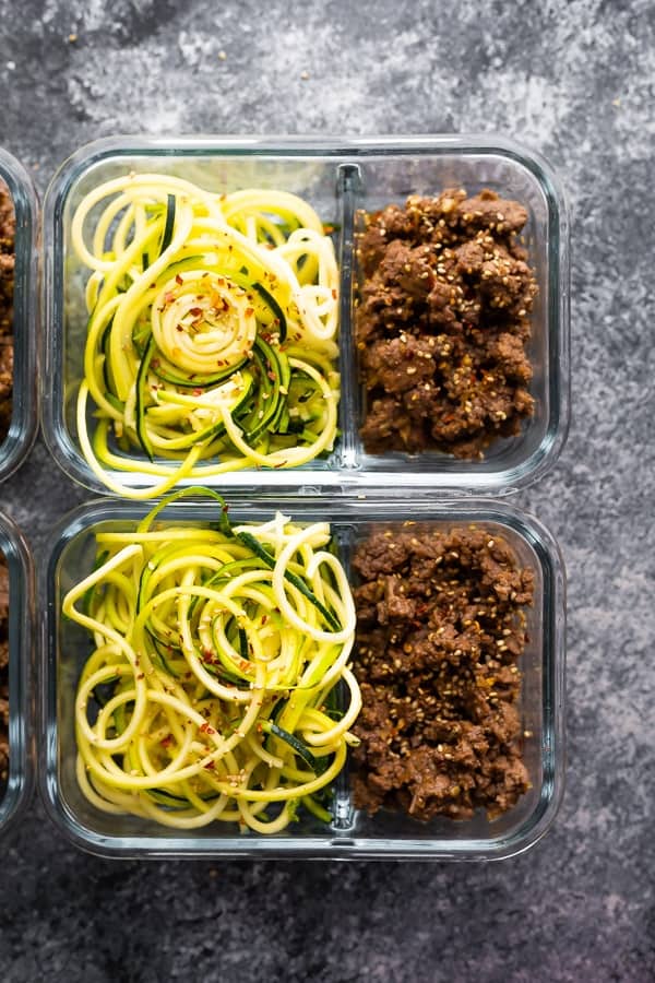 overhead shot of glass meal prep containers filled with sesame ginger beef and zucchini noodles