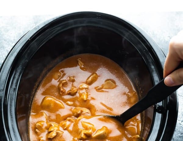 spoon stirring butter chicken in a slow cooker